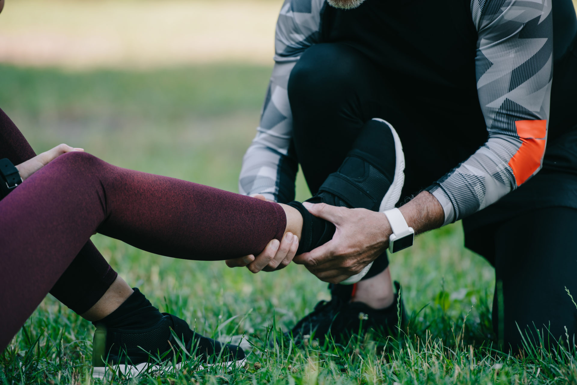 cropped view of sportsman touching injured leg of sportswoman sitting on lawn sports injuries